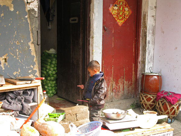 Kid plays with chopstick, Chinese cellery stored in the hallway, fermenting vegetables in pots, huge squash sitting on the sidewalk, knife resting on chopping block